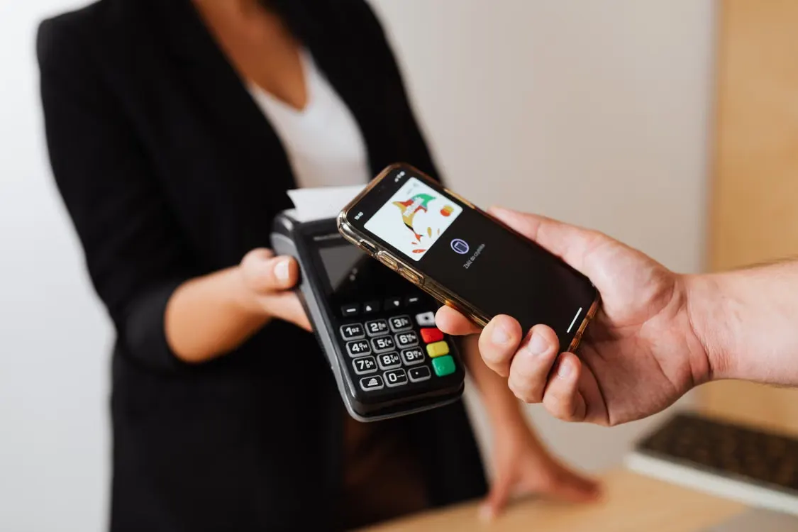 A person using a smartphone to make a contactless payment at a point-of-sale terminal.