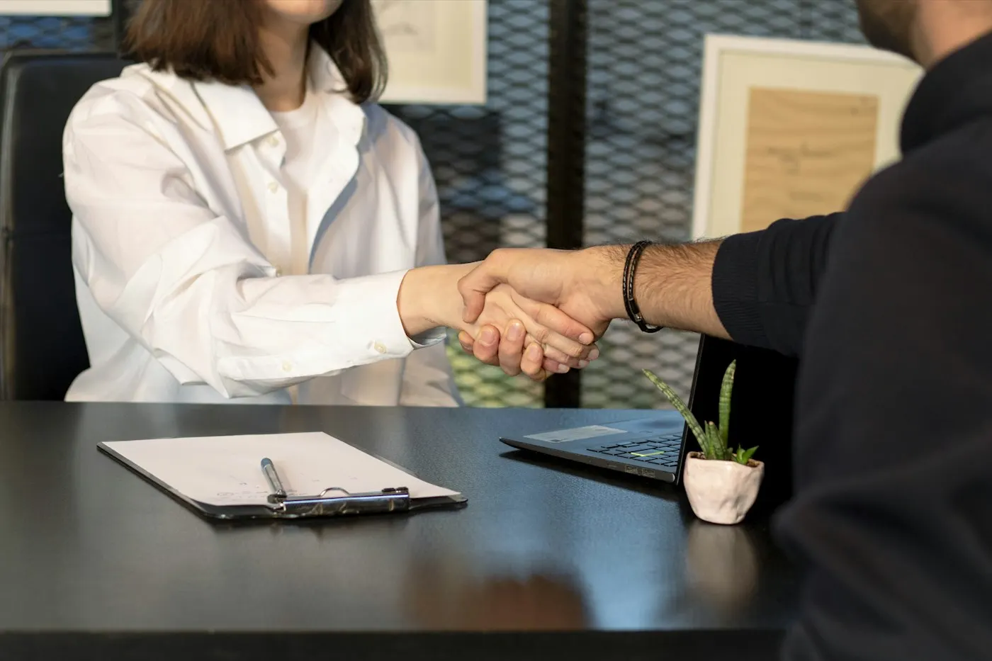 Two people shaking hands over a contract on a table
