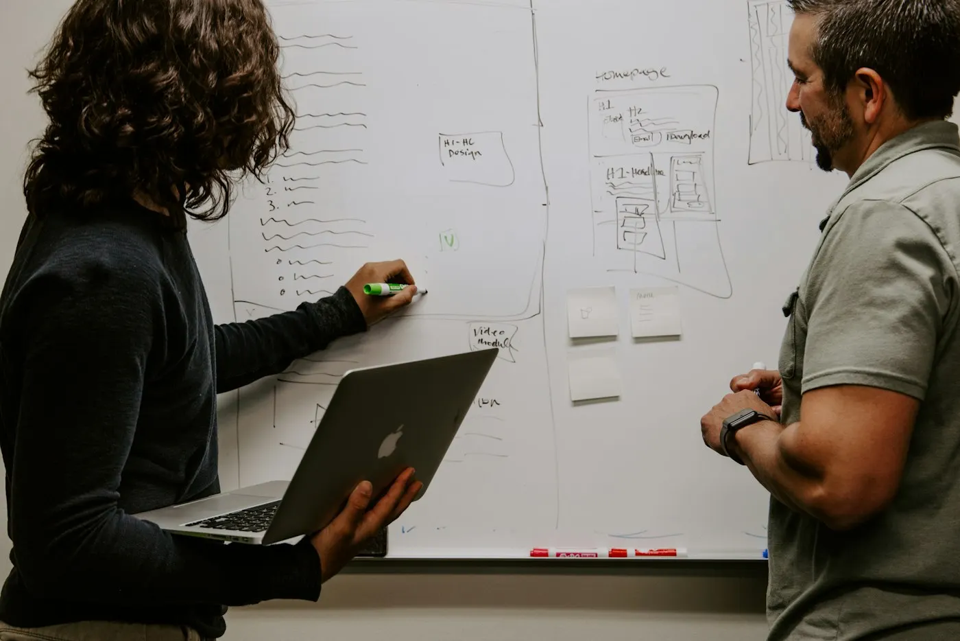 Two developers discussing a diagram on a whiteboard