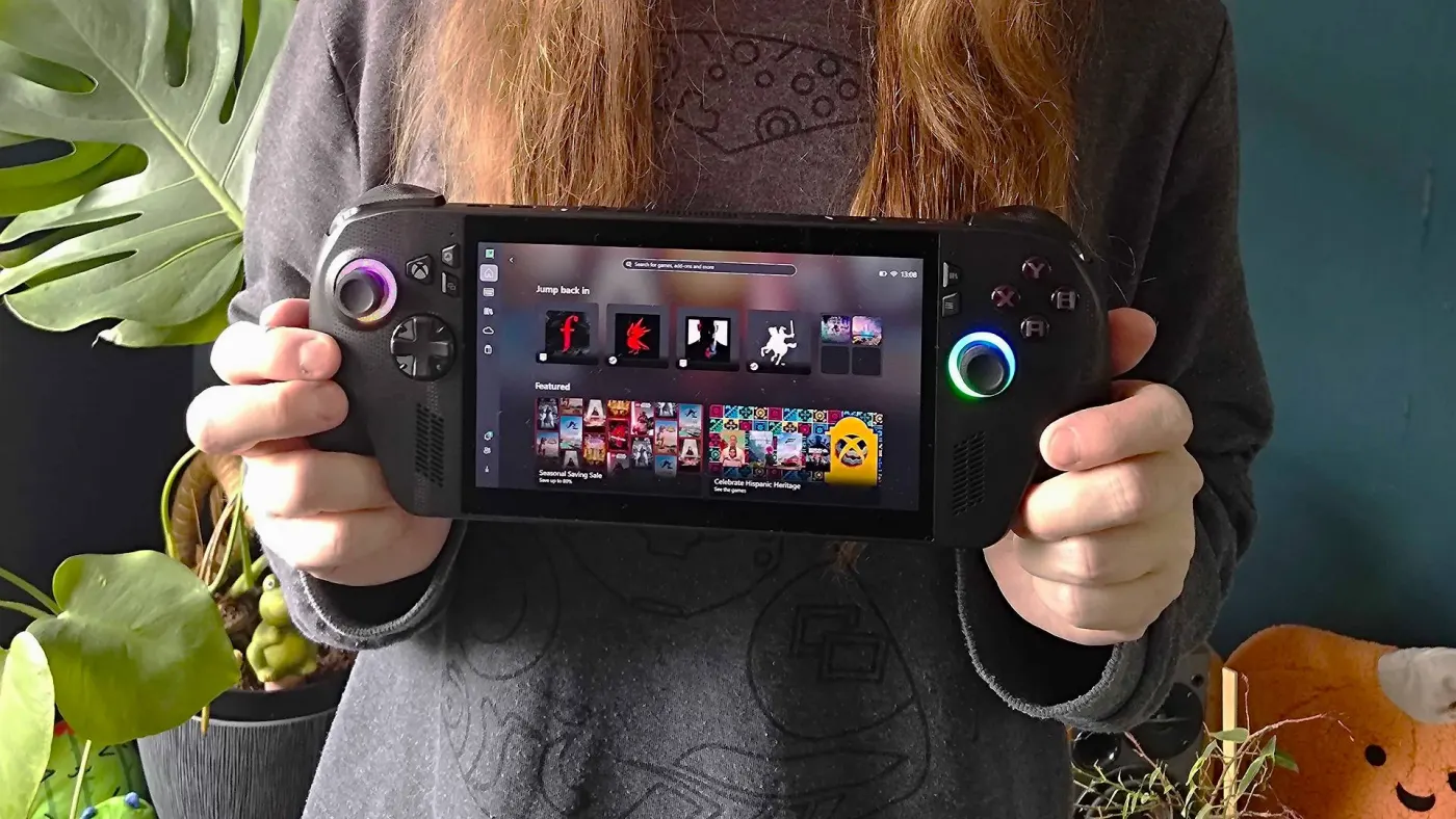A handheld gaming PC held in two hands at a trade show, with a game visible on the display.
